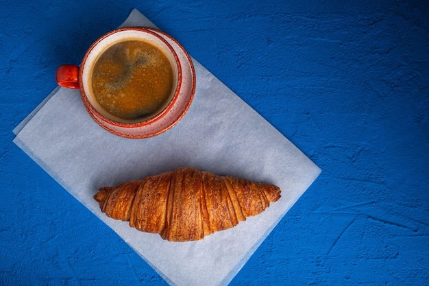 Caffè in tazza e croissant su un tavolo blu