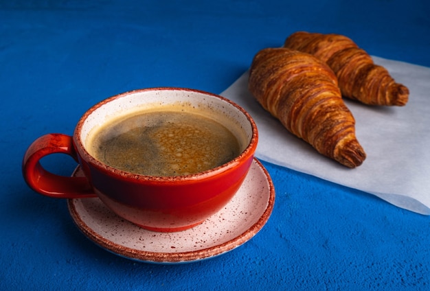 Caffè in tazza e croissant su un tavolo blu