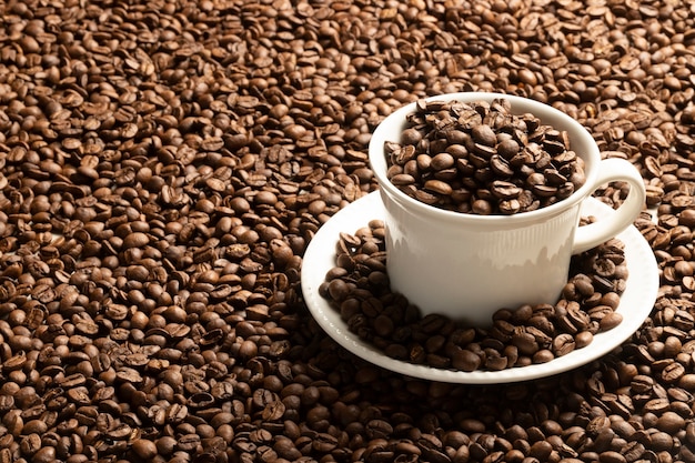 Фото Чашка кофе заполнена кофейными зернами на столе с разбросанными кофейными зернами.