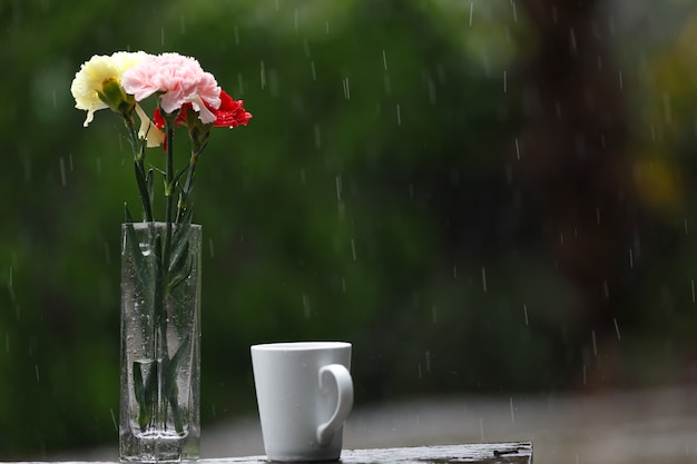 Foto tazza di caffè e vaso di fiori messi in giardino in una giornata piovosa.