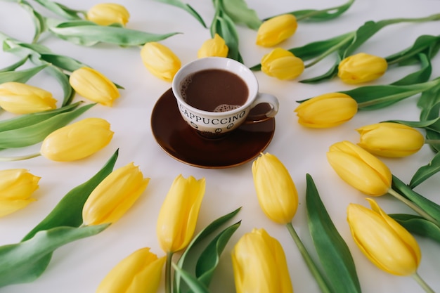 A coffee cup in a frame of tulips on white.