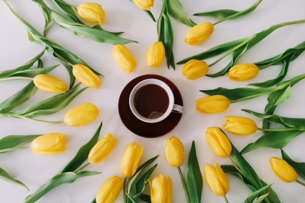 A coffee cup in a frame of yellow tulips on white.