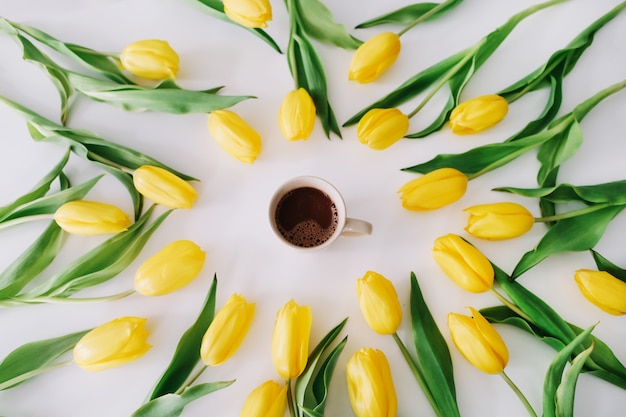 A coffee cup in a frame of yellow tulips on white.