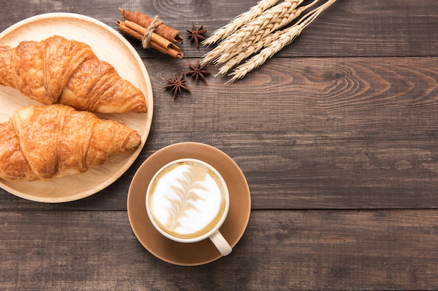 Coffee cup and fresh baked croissants on wooden background. Top View