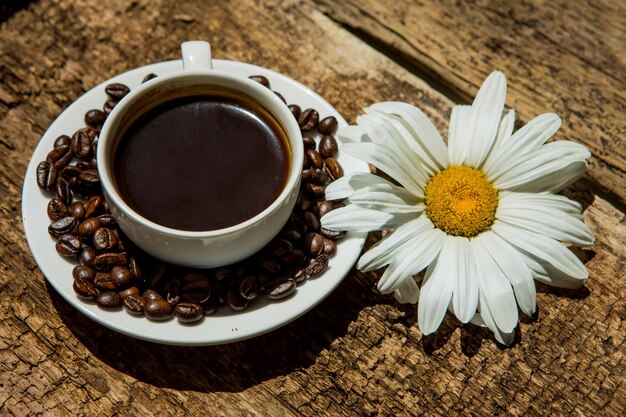 Coffee cup and fried Coffee beans on a wooden table with beautiful white flowers on a wood background