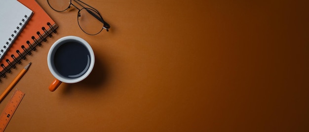 A coffee cup glasses and notebook on orange leather with cop space