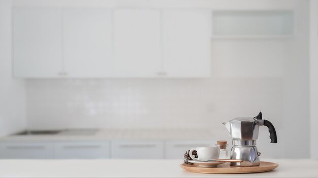 Tazza di caffè e moka in vassoio di legno sul bancone bianco con sfondo sfocato cucina