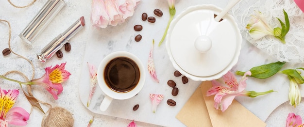 Coffee cup near pink flowers on white table