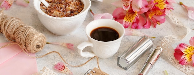 Coffee cup near pink flowers on white table