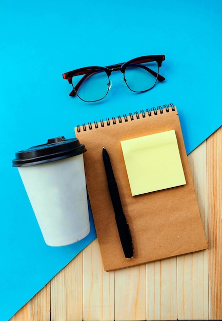 Coffee cup notebook and glasses on a blue background