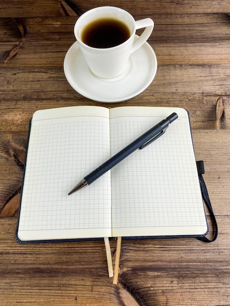 Coffee in a cup and a notebook with a pen Vertical photo