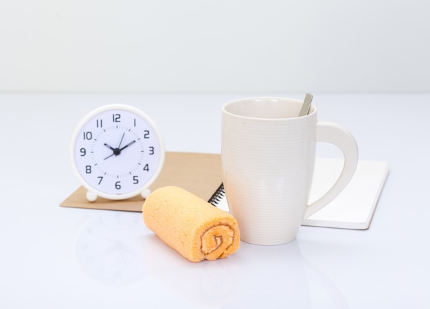 Coffee cup and orange roll cake with office accessories background