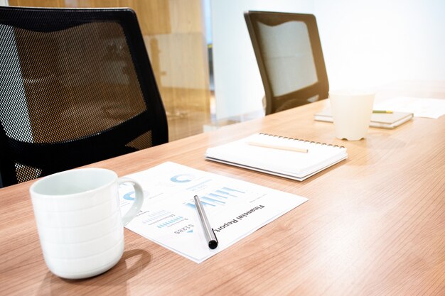 Coffee cup and paperwork on table with two black armchairs in meeting room