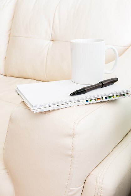 Coffee cup, pen, notebook is on white sofa