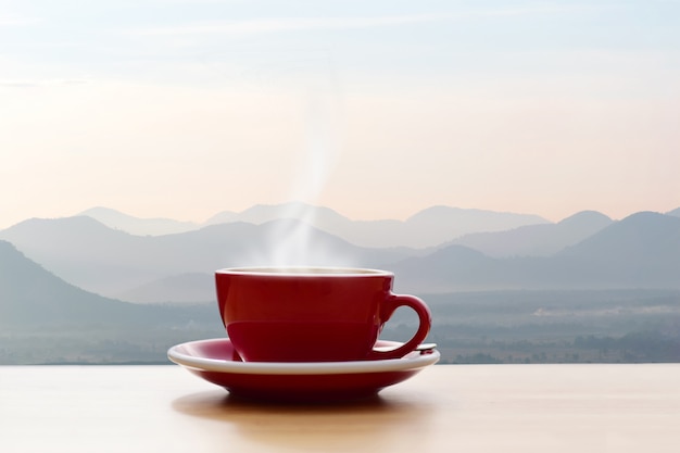 朝の太陽の光の山の景色と赤のコーヒーカップ