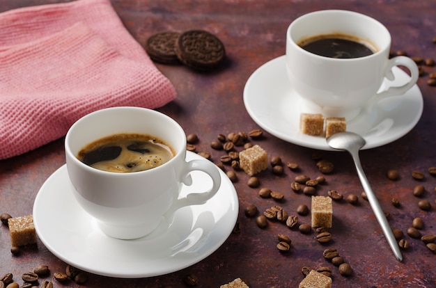 Coffee in cup and saucer on dark background with coffee beans and cane sugar.