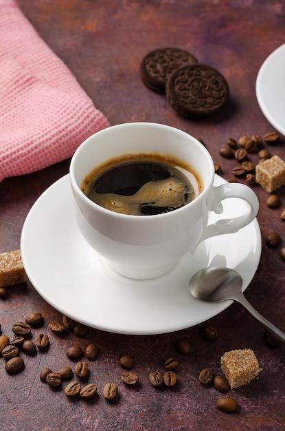 Кофе в чашке и блюдце на темном фоне с кофейными зернами и тростниковым сахаром.