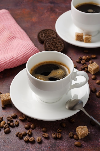 Caffè in tazza e piattino su sfondo scuro con chicchi di caffè e zucchero di canna.