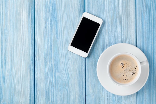 Coffee cup and smartphone on wooden table background