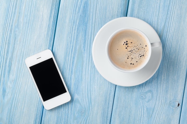 Coffee cup and smartphone on wooden table background