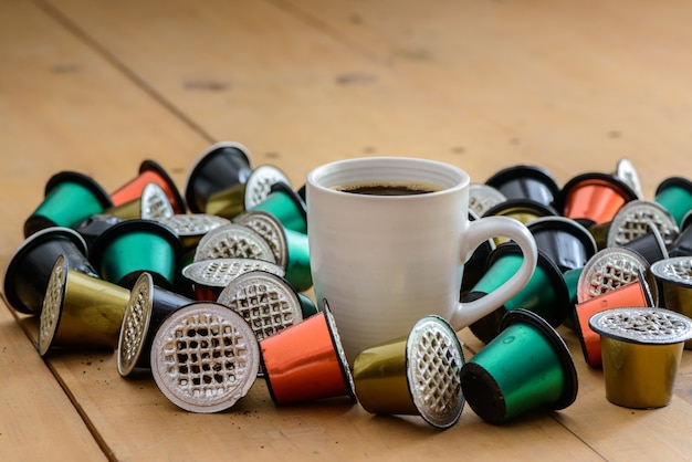 Coffee cup surrounded by used coffee capsules on wooden table