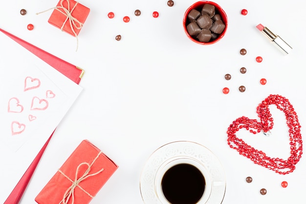 Coffee cup, sweets, lipstick, heart shape and giftbox on white background. Valentine's Day concept frame.