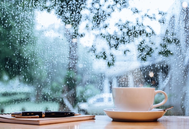 雨季の窓の向こうのテーブルの上のコーヒーカップ