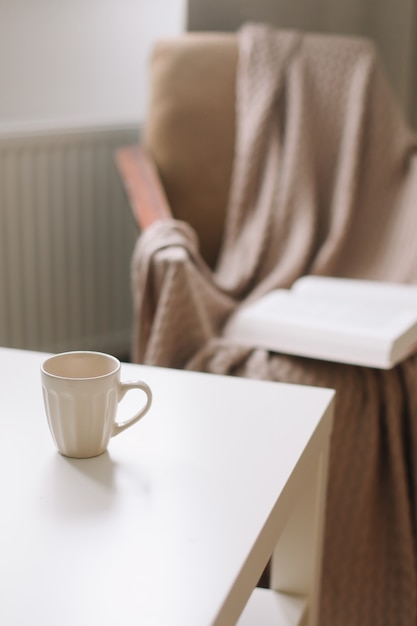 coffee cup on a table next to armchair with open book