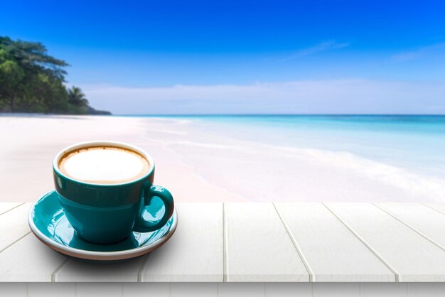 Coffee cup on table by sea against blue sky