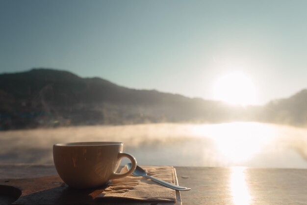 Photo coffee cup on table with lake and lake in background during sunrise