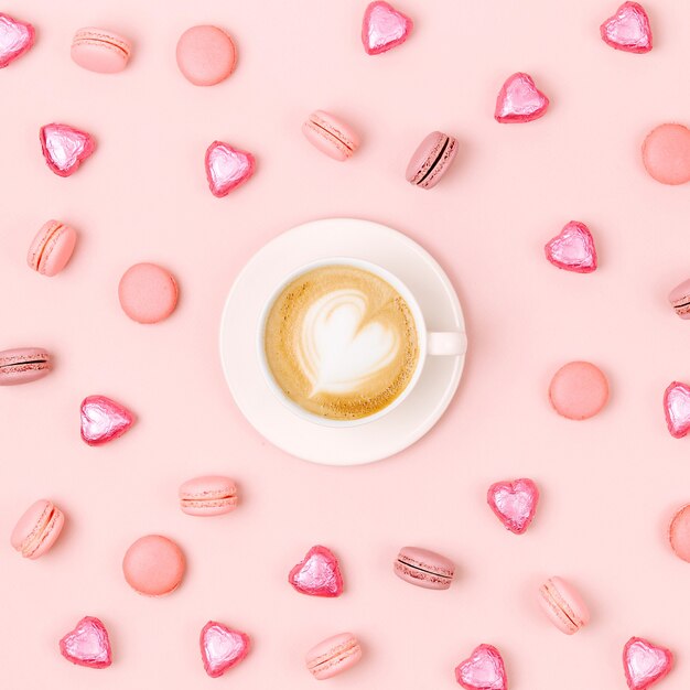 Coffee cup with candys and macaroons on pale pink background. Flat lay, top view