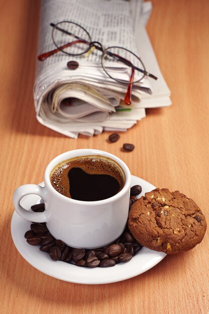 Coffee cup with chocolate cookie and newspaper on desk