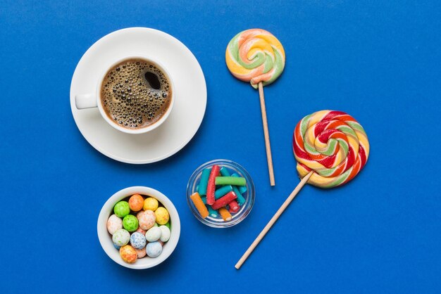 Coffee cup with chocolates and colored candy top view on table background with copy space