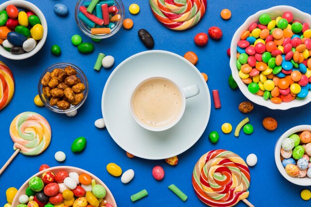 Coffee cup with chocolates and colored candy top view on table background with copy space