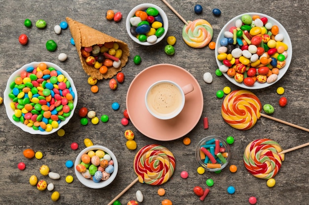 Photo coffee cup with chocolates and colored candy top view on table background with copy space