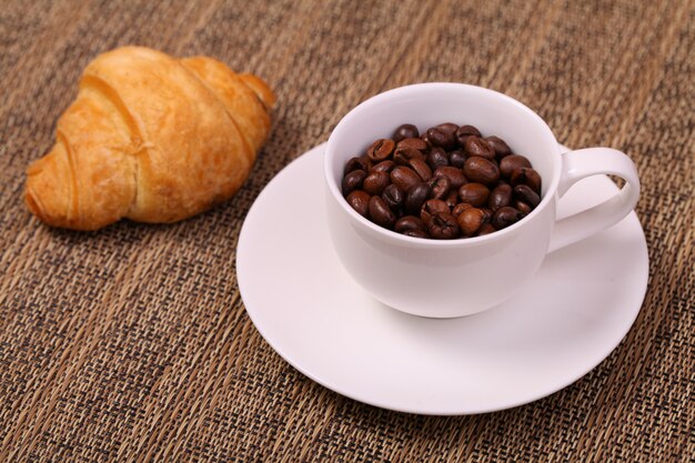 Coffee cup with a croissant and fresh coffee beans