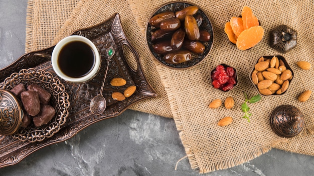 Coffee cup with dates fruit and almonds on metallic tray