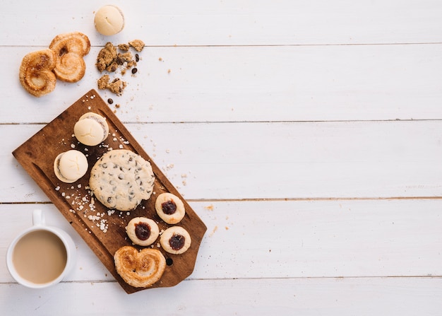 Coffee cup with different cookies on wooden board