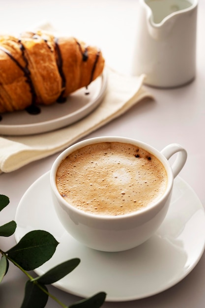 Coffee cup with fluffy milk foam and croissantson bright background Breakfast time