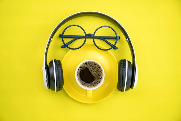 coffee cup with headphone and teacher glasses on yellow paper background