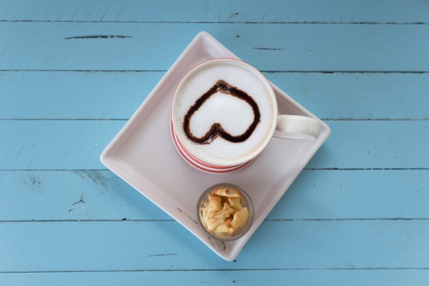 Coffee cup with heart latte art on blue wooden board