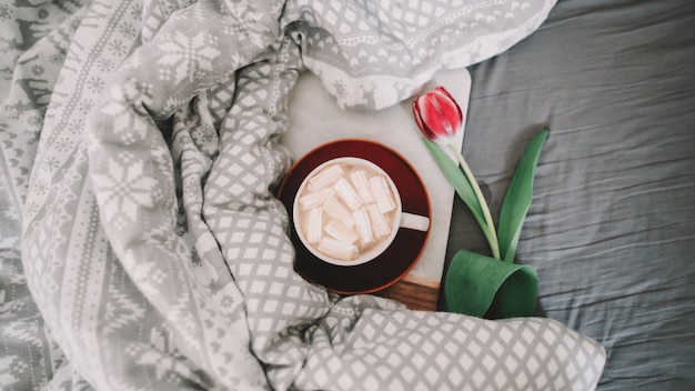 Coffee cup with marshmallows and red tulips in bed. Concept of holiday, birthday, Valentines Day, March 8