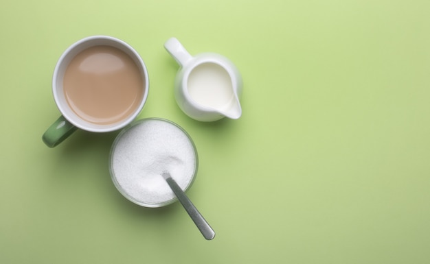 Coffee in a cup with milk with a milk jug and a bowl with a spoonful of sweetener. Copy space