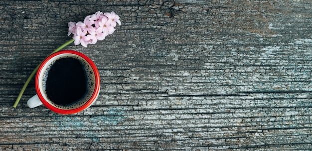 Photo coffee cup with red border and pink hyacinth flower on old wood background. copy space. top view.