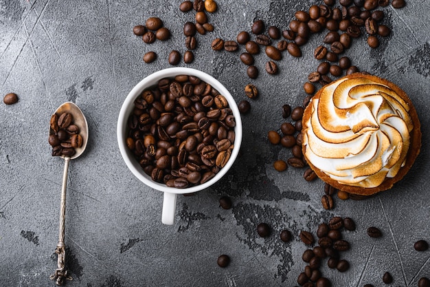 Coffee cup with roasted beans and cup cake on grey, top view