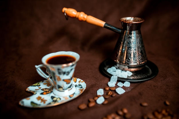 Coffee cup with sugar cubes and coffee beans around. Silver cezve.