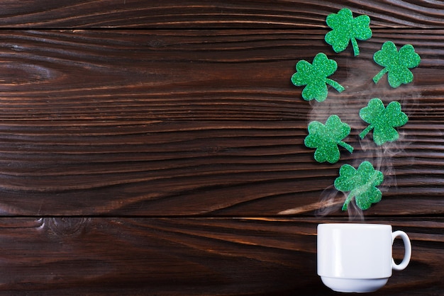 Coffee cup with three leaved shamrock handmade leaves on wooden background