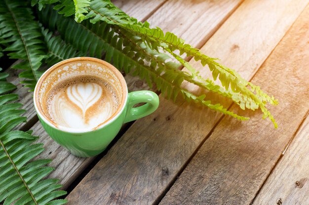 coffee cup on wood table with fern leaf 