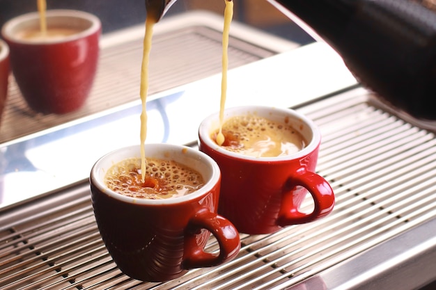 Coffee cups stand inside the coffee machine on a grid, fresh coffee is poured inside the cups