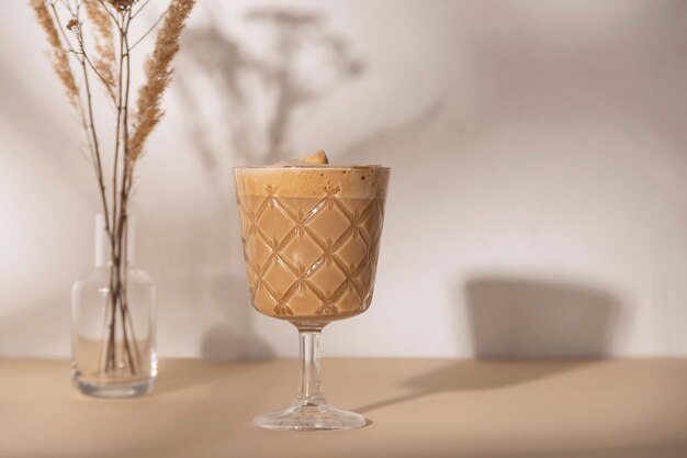 Coffee drink in a stemmed glass with a bouquet of dried flowers on a beige and white neutral background with shadows from the summer sun. Background with copy space